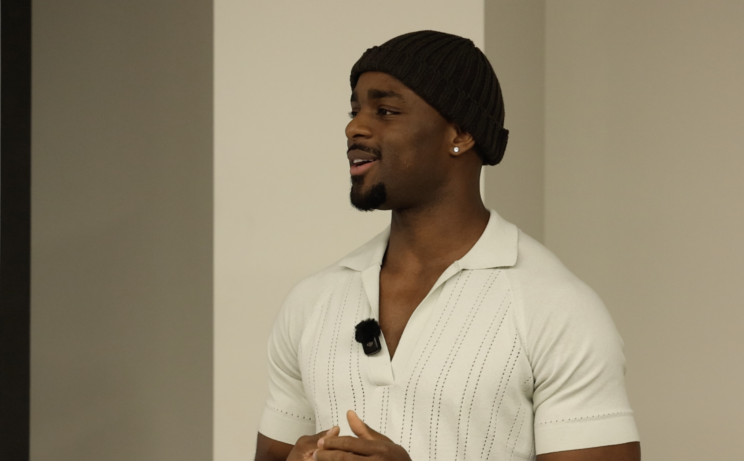 Speaking on stage in a white shirt and beanie